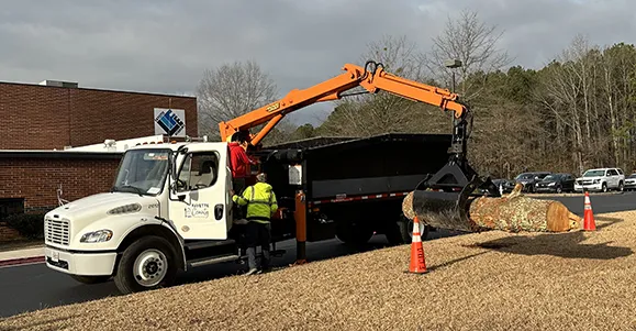 Road Department Grapple Truck with a student operating it while a Road Department Worker supervises.
